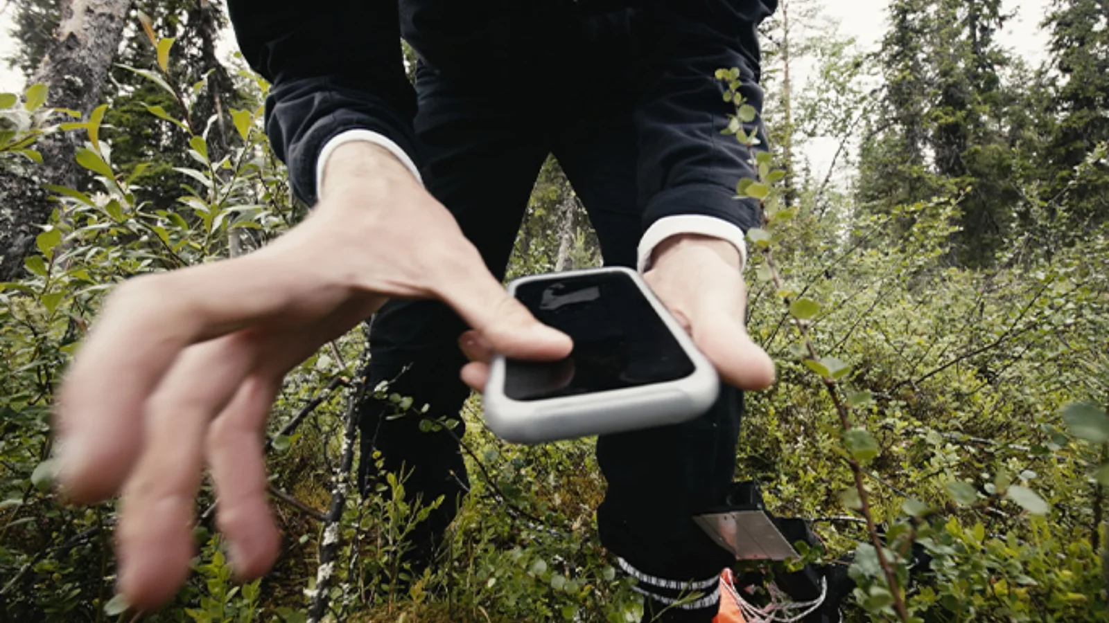 Pessoa segurando o iPhone 17 Pro recuperado numa floresta no norte da Suécia, ainda dentro da capa