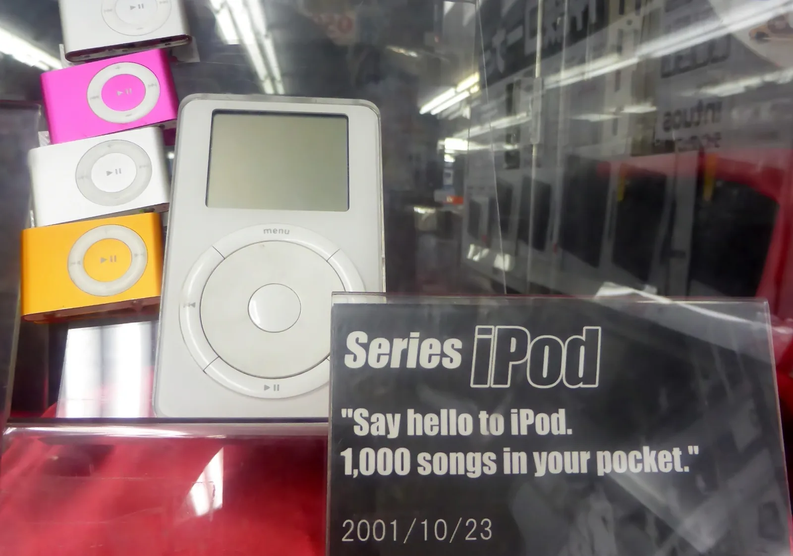 iPod de primeira geração em exposição ao lado de iPod shuffle coloridos e uma placa com a data de 23 de outubro de 2001